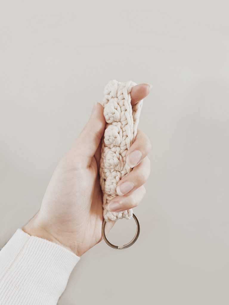 A white crocheted wristlet being held by a hand.