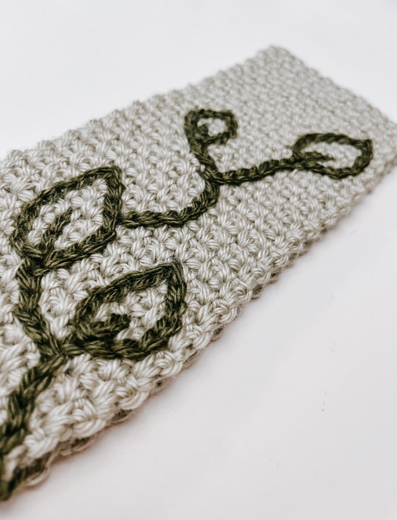 A silver headband with green leaves crocheted on the front. 