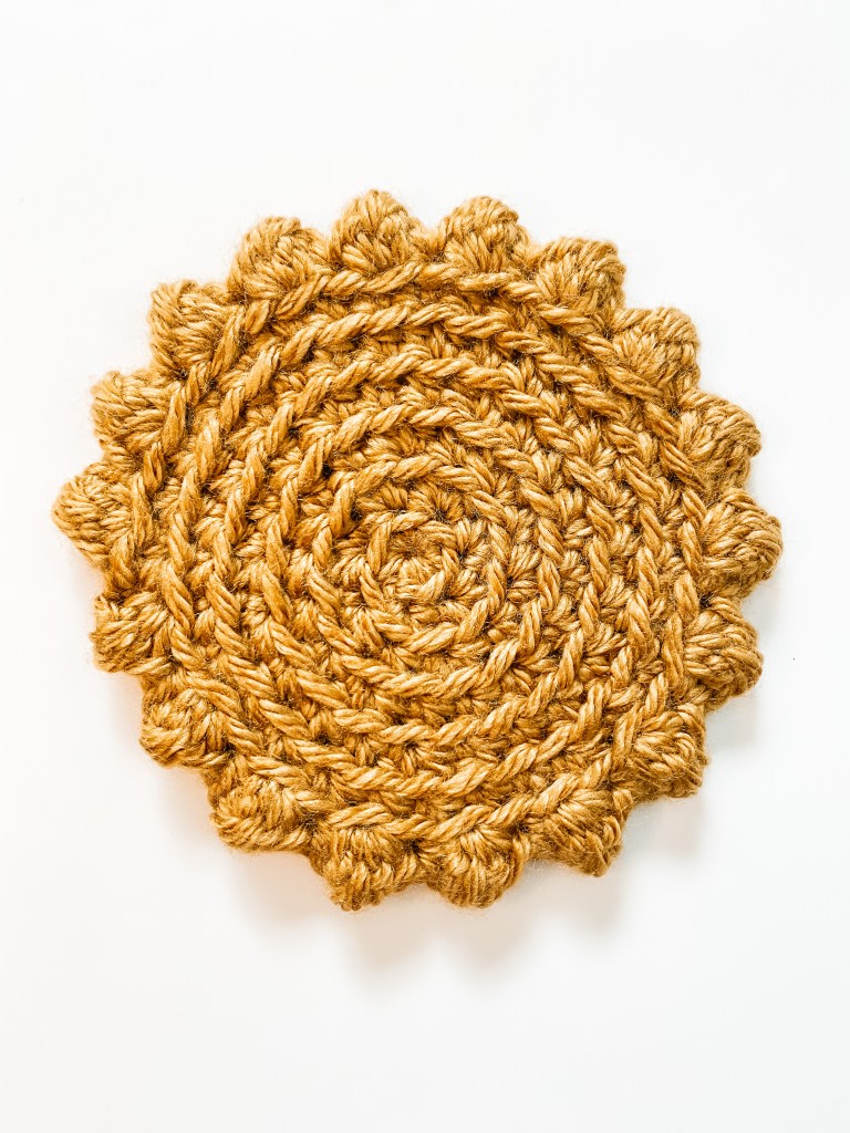 A gold drink coaster with a spiral and crocheted texture.